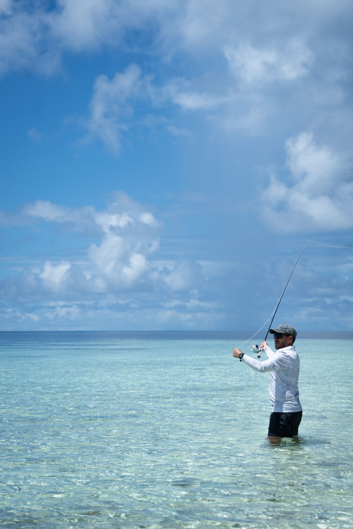 Angler fly fishing in crystal clear turquoise waters under a blue sky.