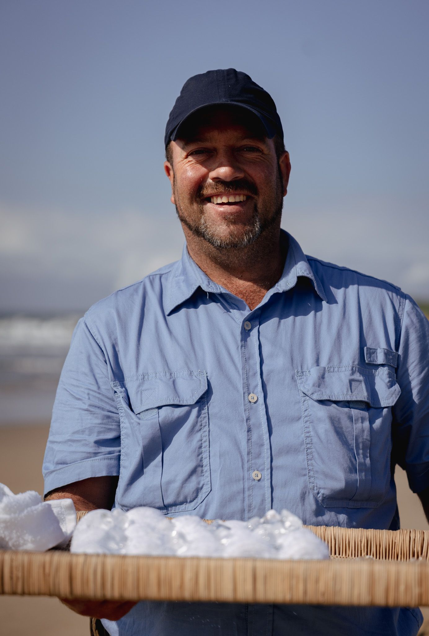Server holding a tray of fresh oysters on ice outdoors by the beach.