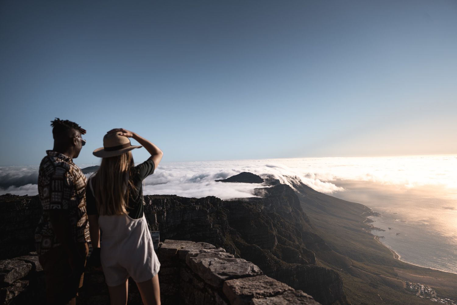 Silhouetted figures watching sunset from mountain overlook with dramatic cloudscape.