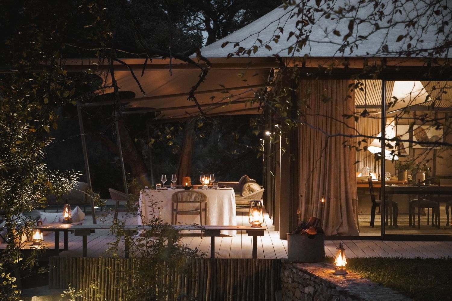 Outdoor seating area at dusk with glowing lanterns and string lights creating an intimate atmosphere.