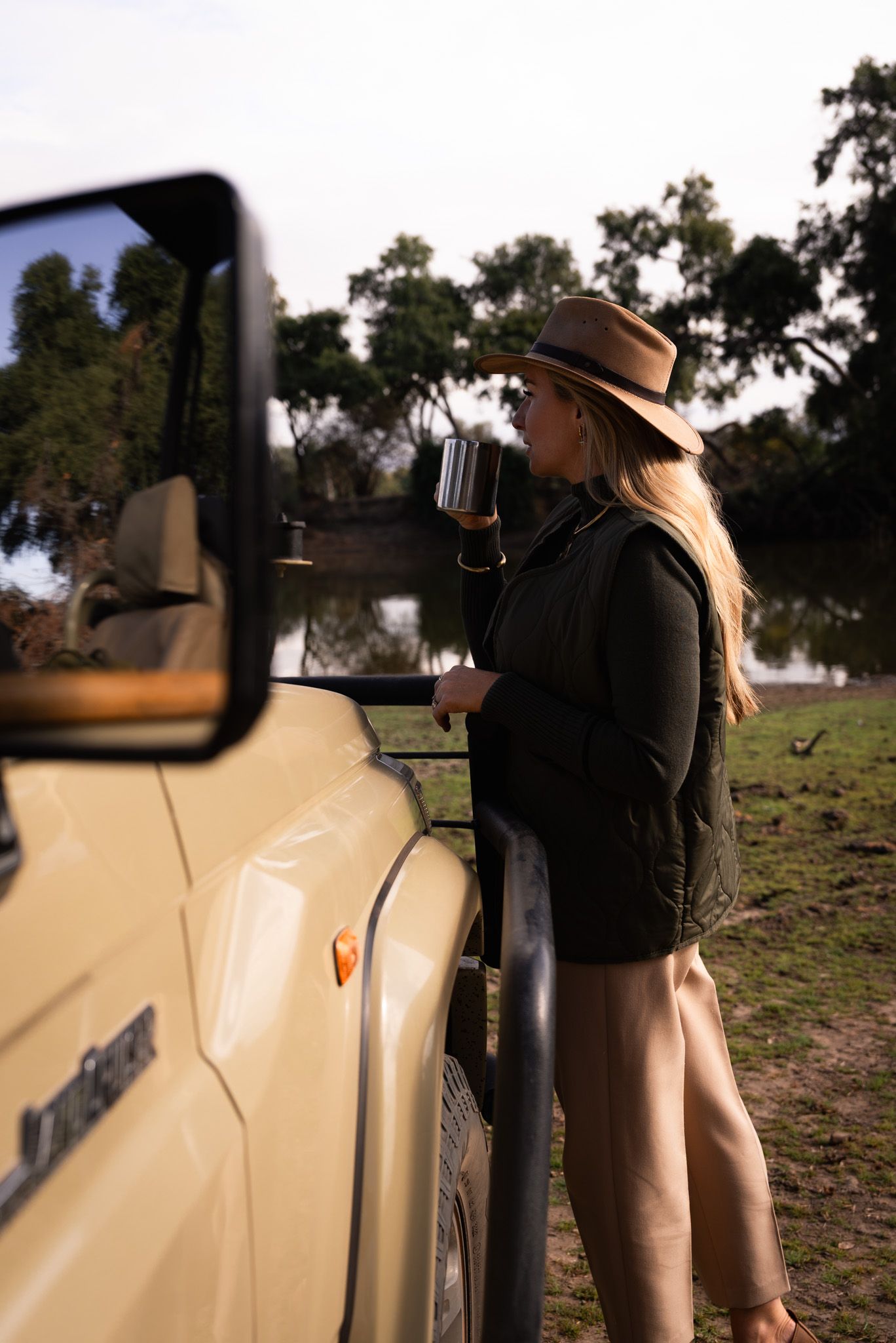 Safari vehicle side view with adventurers in bush hats against natural landscape.