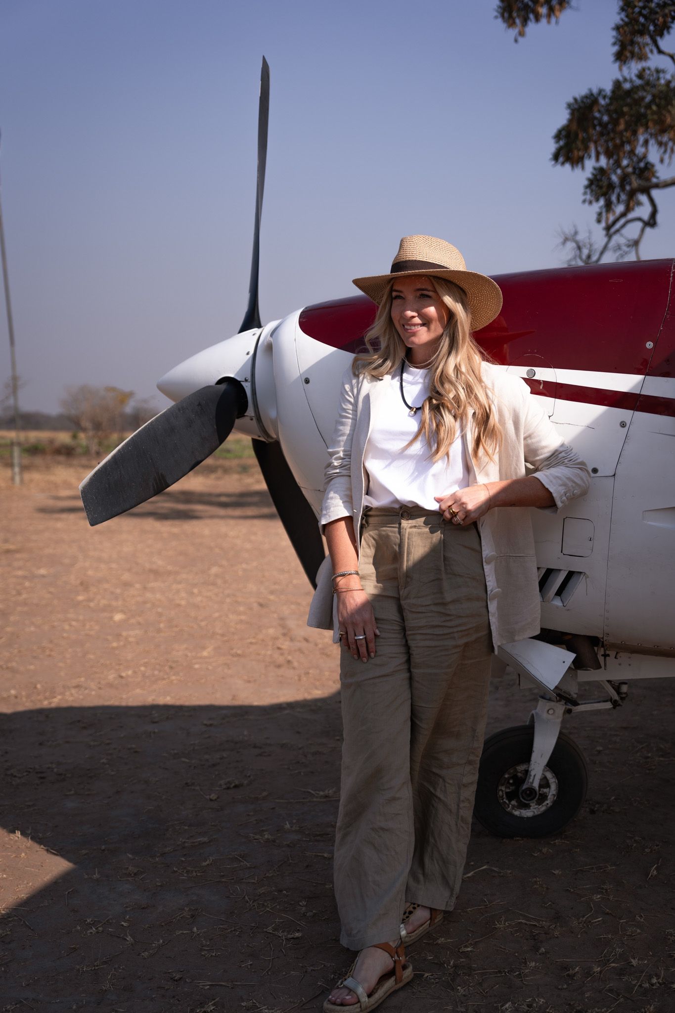Person in casual attire poses next to small private aircraft on dusty airstrip.