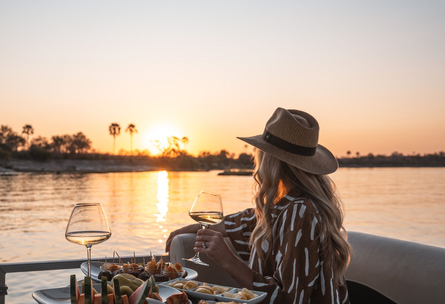Scenic sunset view over water with wine glasses and snacks in foreground.