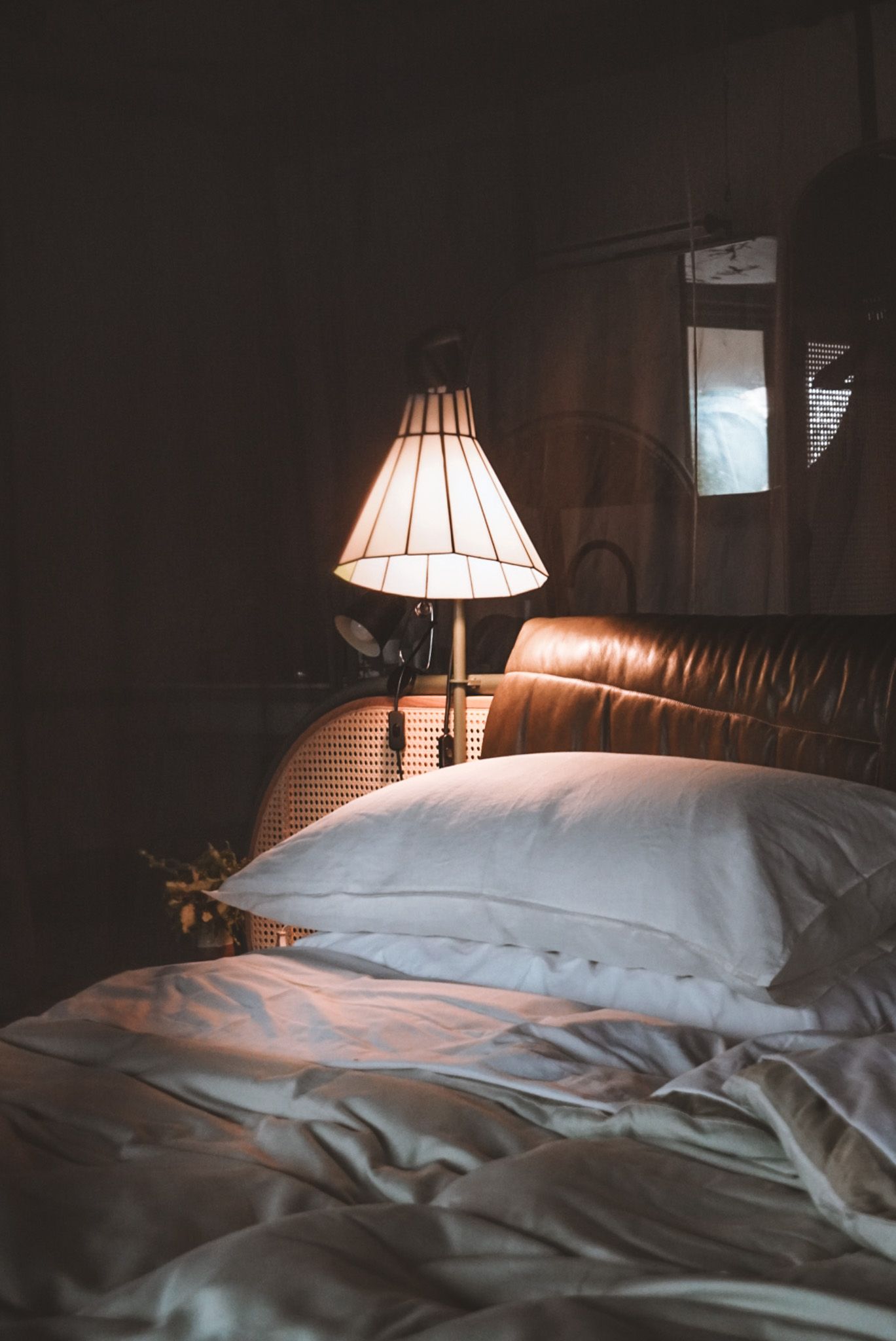 Cozy bedroom scene with soft lamplight illuminating white pillows and bedding.