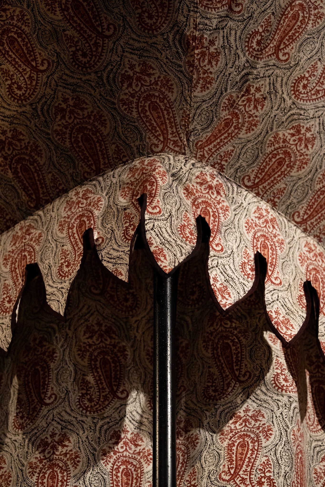 Red and white paisley patterned curtains casting intricate shadows on interior wall.