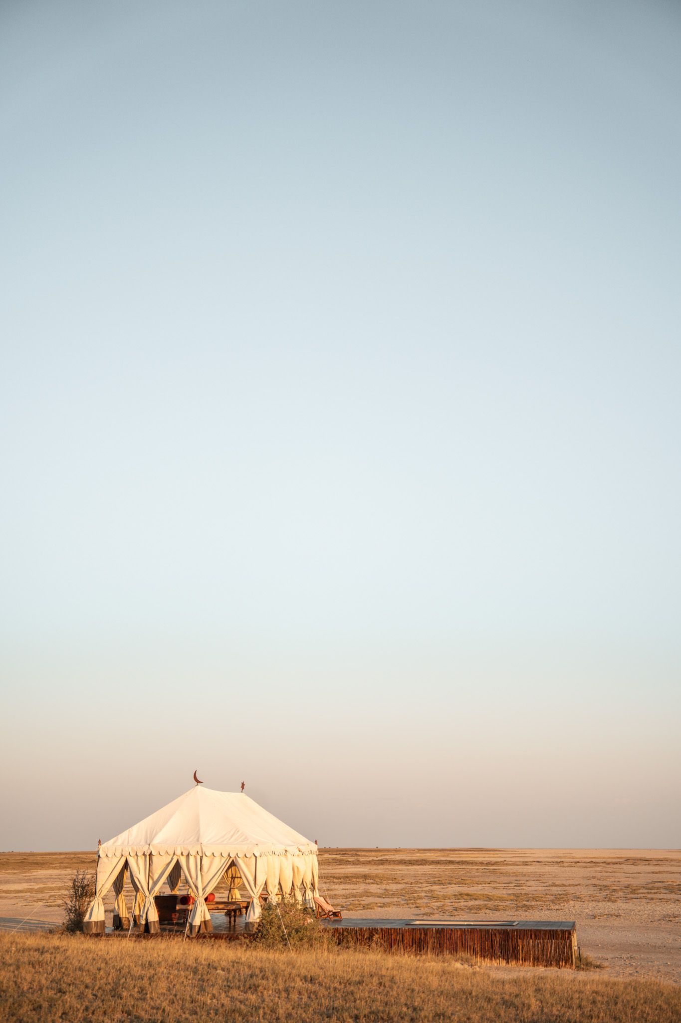 Large white safari tents set up in a vast open grassland under clear blue sky.