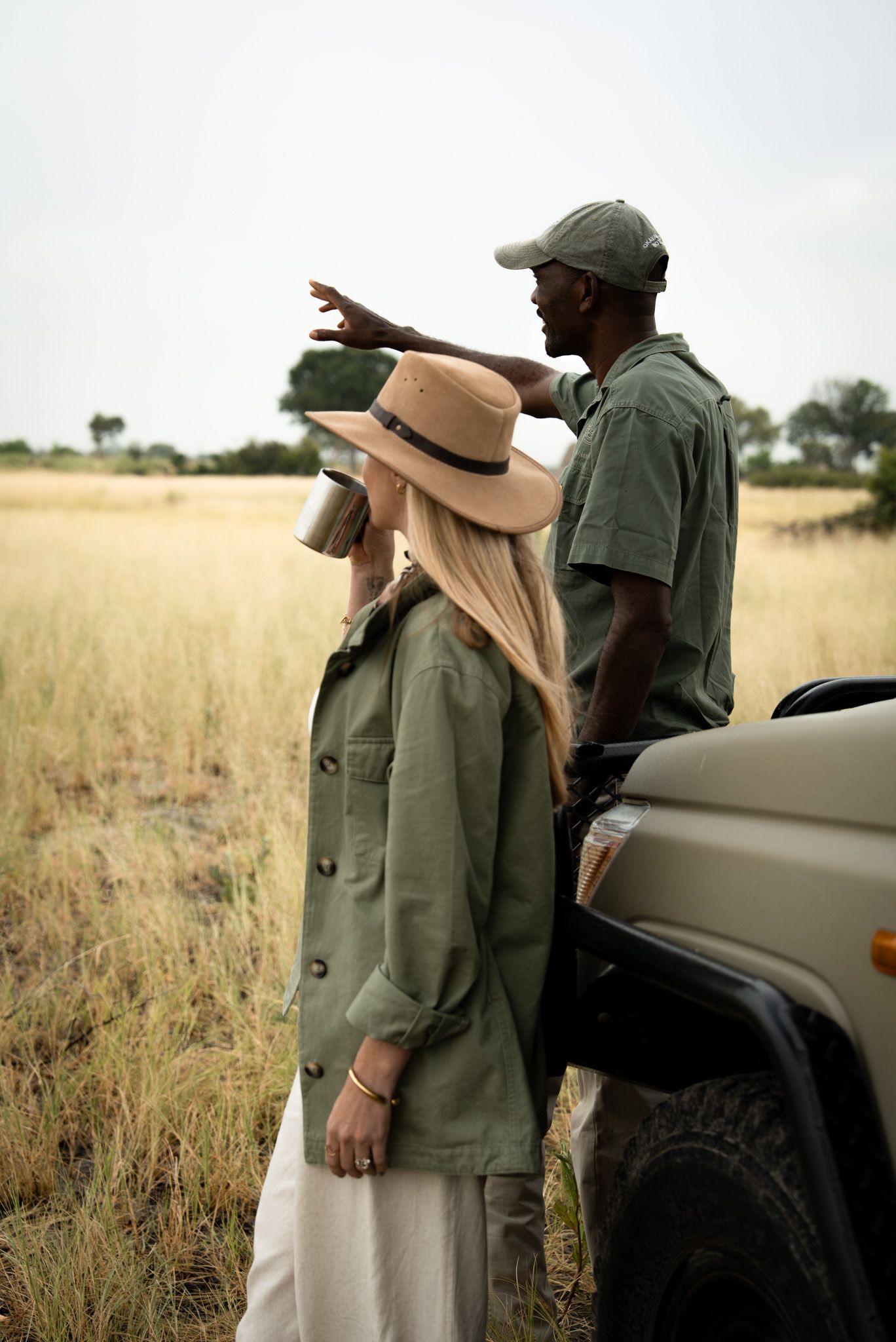 Safari guides pointing out wildlife from a vehicle in tall grass.