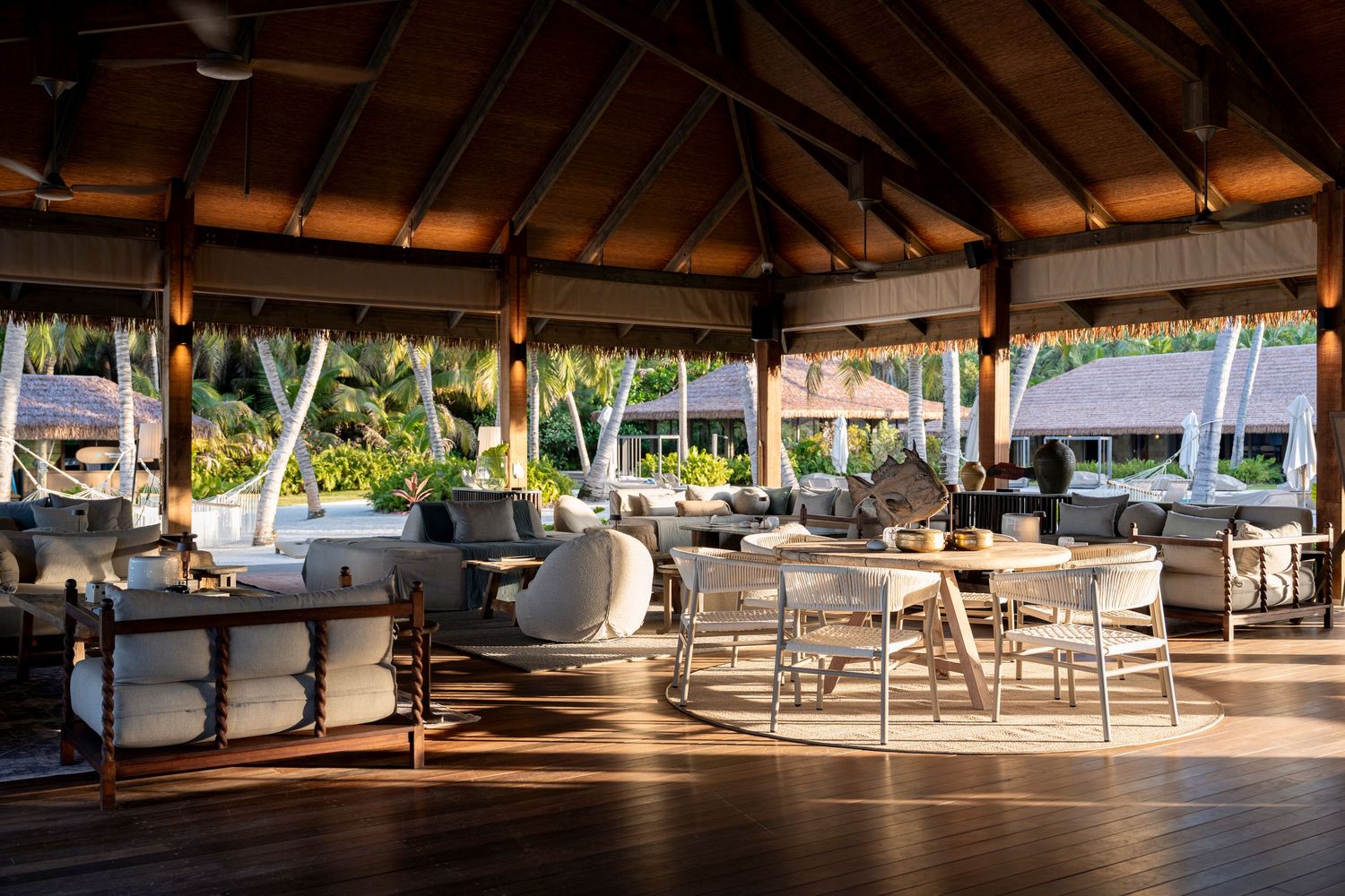 Elegant open-air tropical resort lounge with wicker furniture, wooden ceiling, and lush palm tree views.