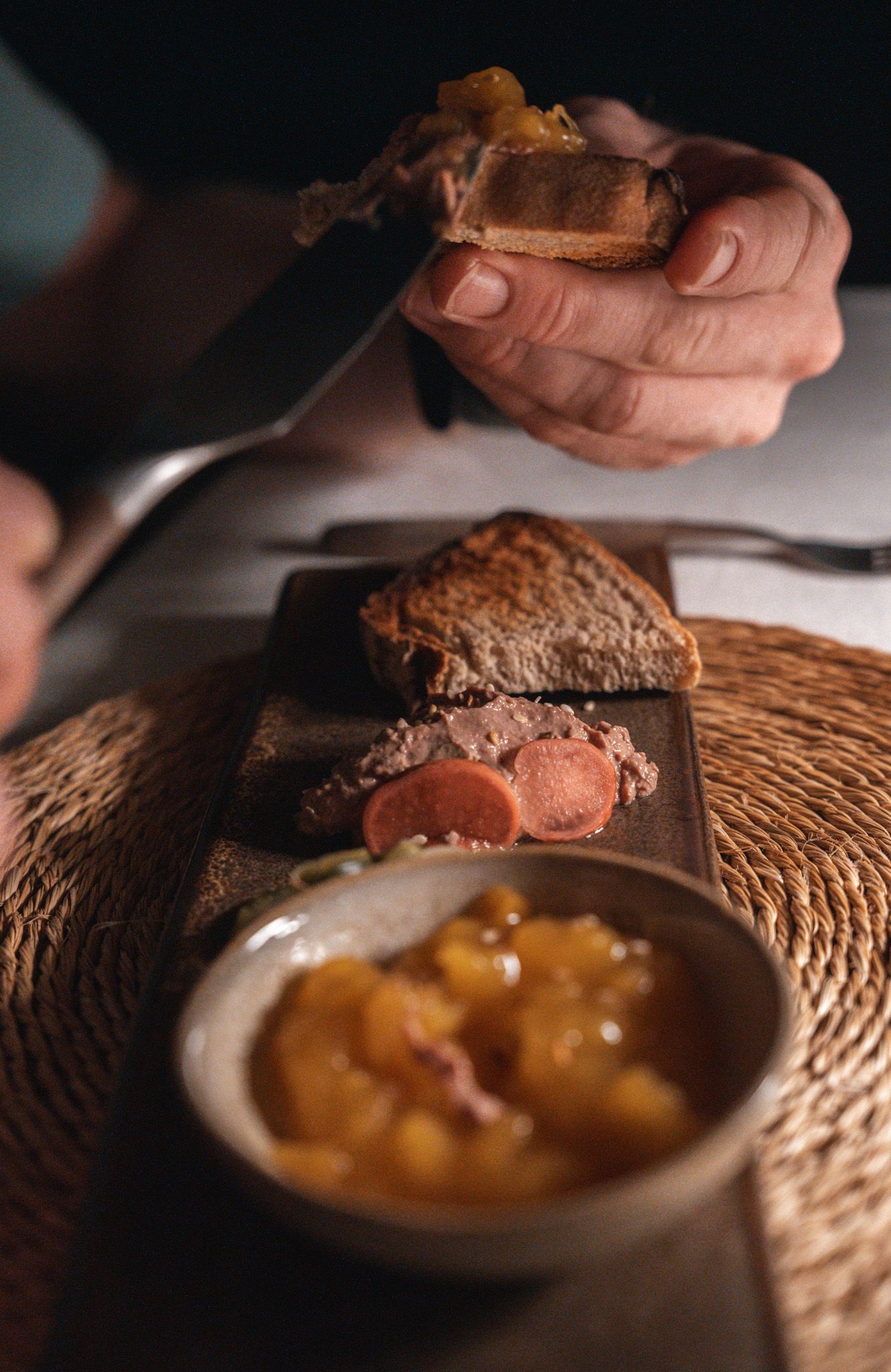 Hands serving a gourmet dessert garnished with caramel sauce on a rustic woven placemat.