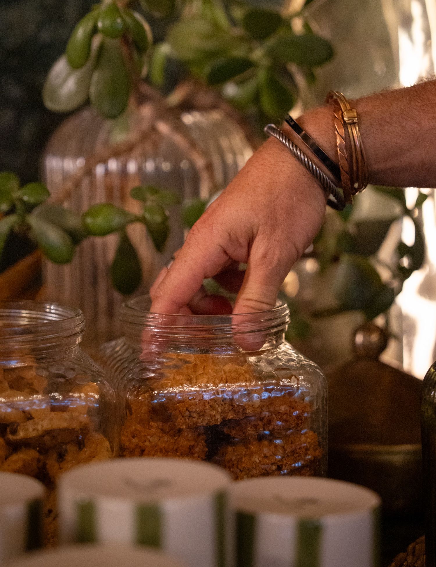 Hand with bracelets reaching into glass jar with granola or trail mix.