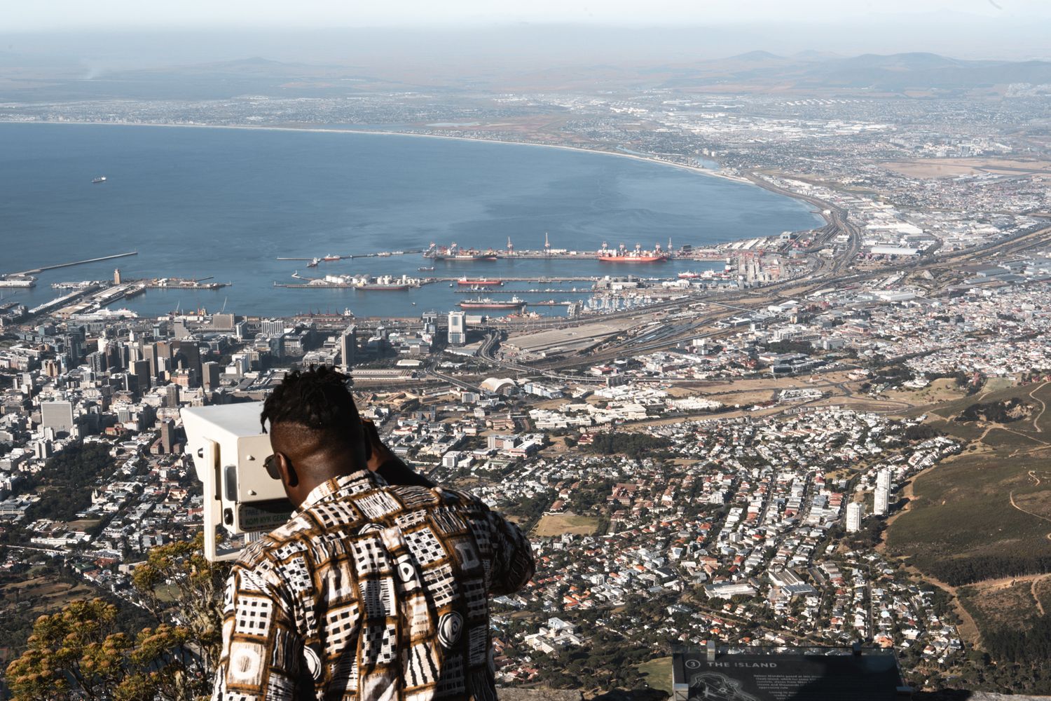 Scenic overlook of a coastal city harbor and mountainous landscape.