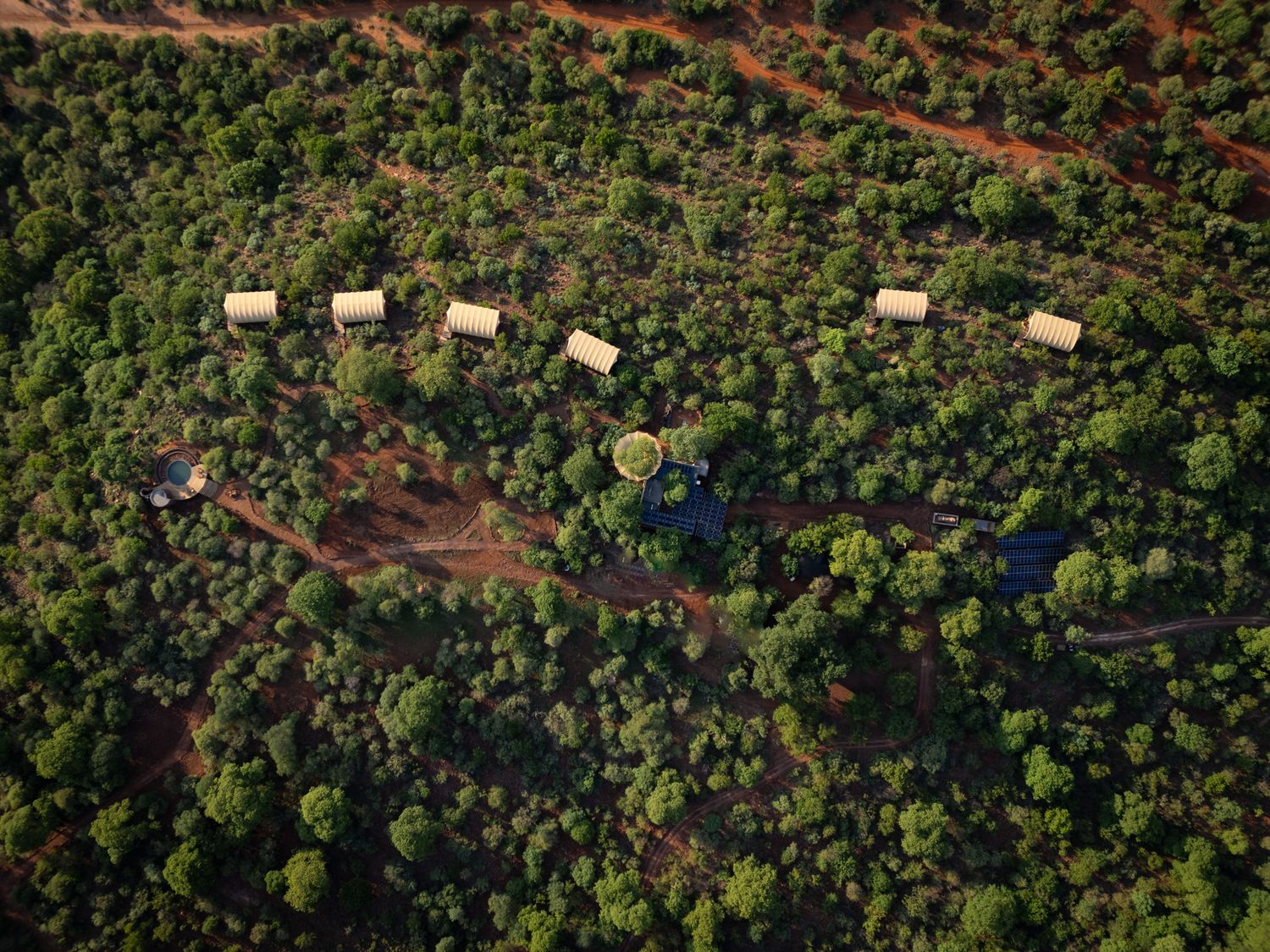 Birds-eye view of luxury safari lodges scattered among dense green forest.