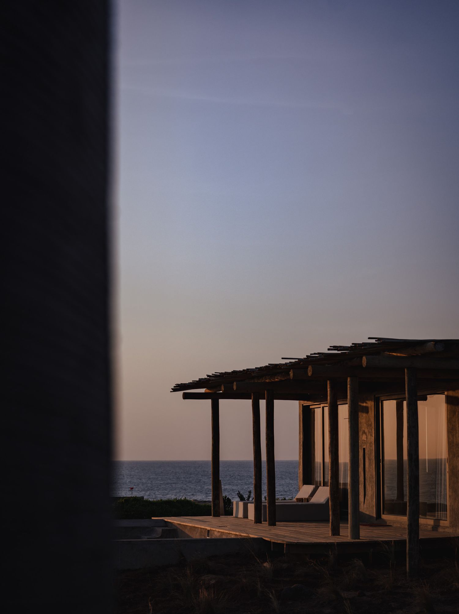 Beachfront pergola structures silhouetted against sunset sky along coastline.