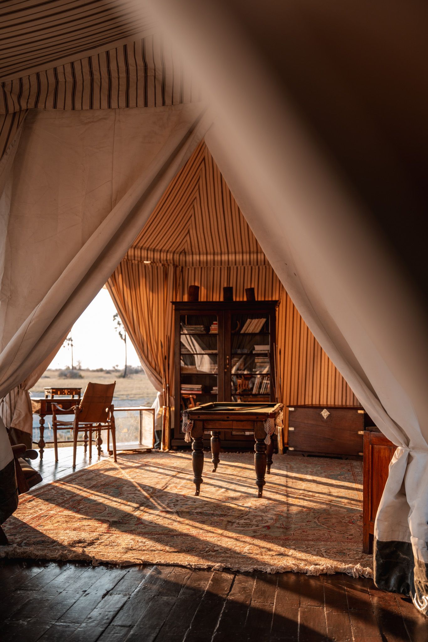 Interior view of a luxury safari tent lodge with wooden furniture and natural light streaming through white canvas walls.