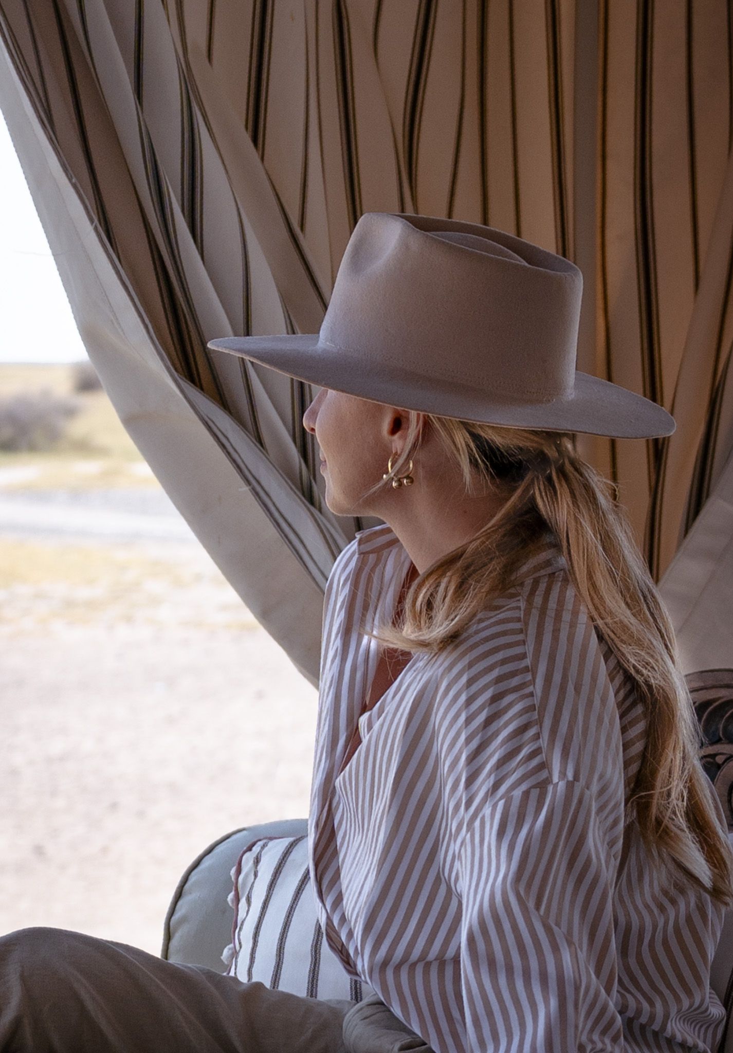 Side view of someone wearing a fedora hat and striped shirt while relaxing in a safari tent.