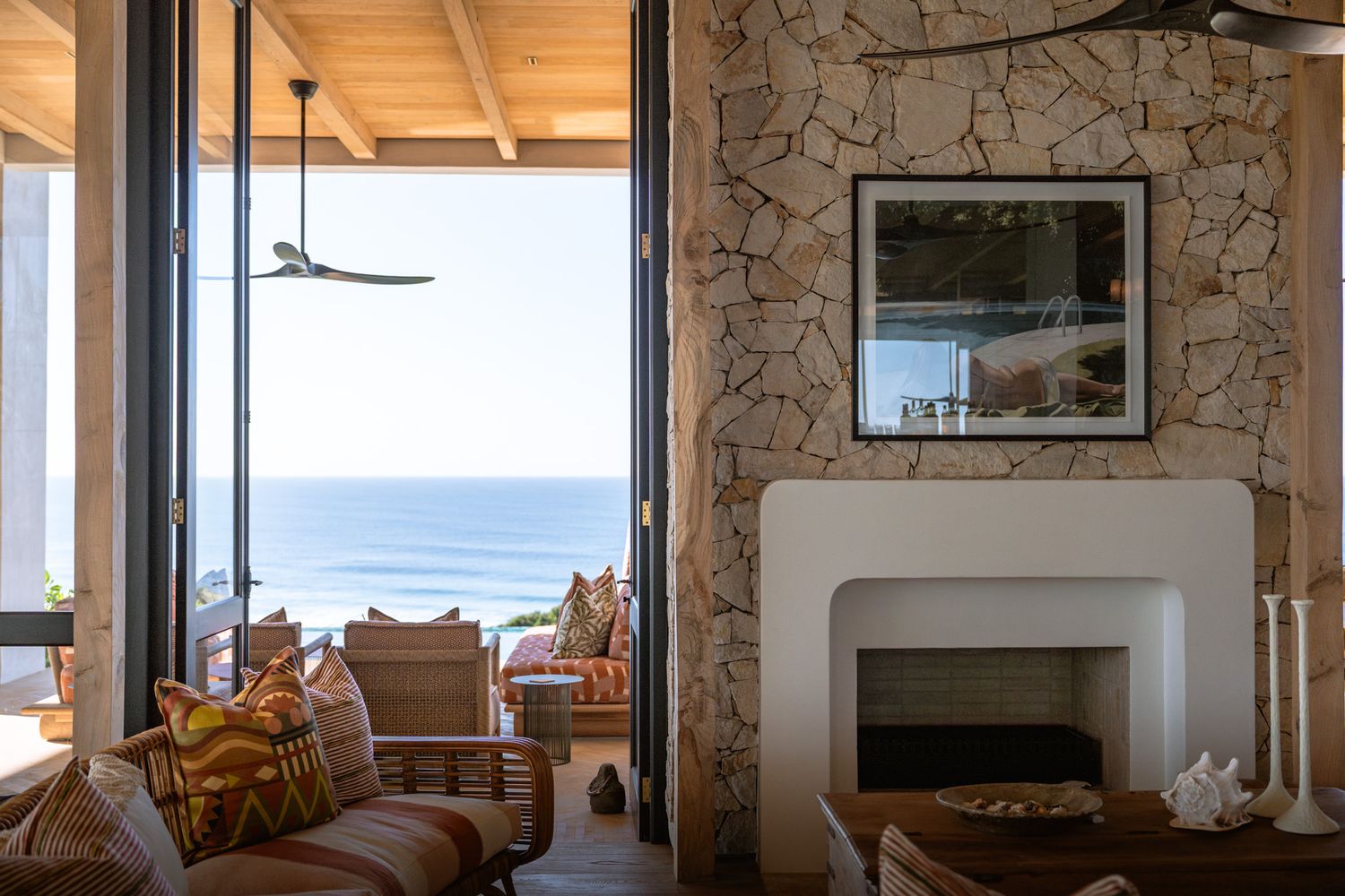 Coastal living room with stone walls and large windows offering panoramic ocean views.