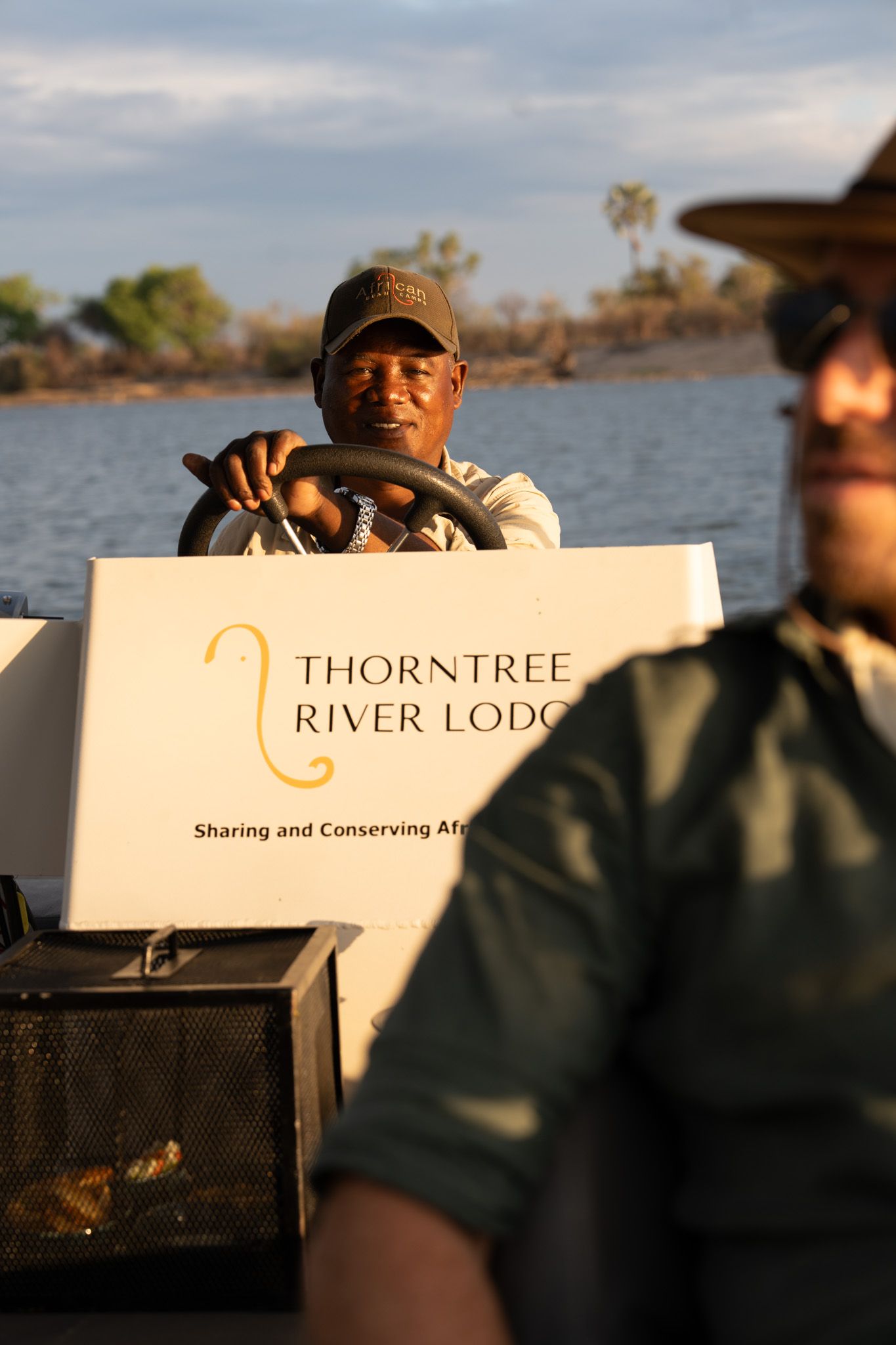 Staff member at helm of Thorntree River Lodge boat during river excursion.