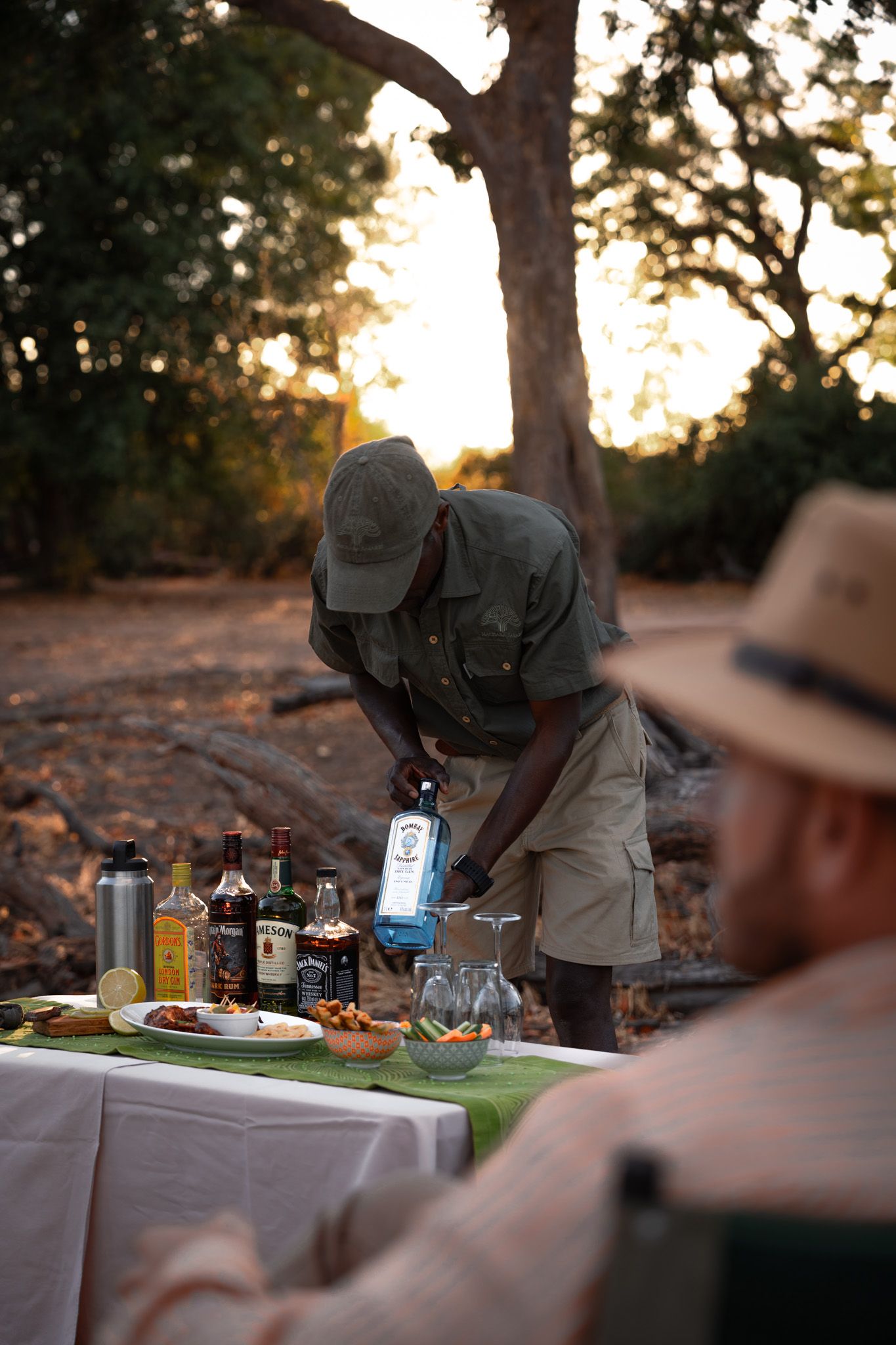 Outdoor dining setup with white tablecloth and beverages at dusk under trees.