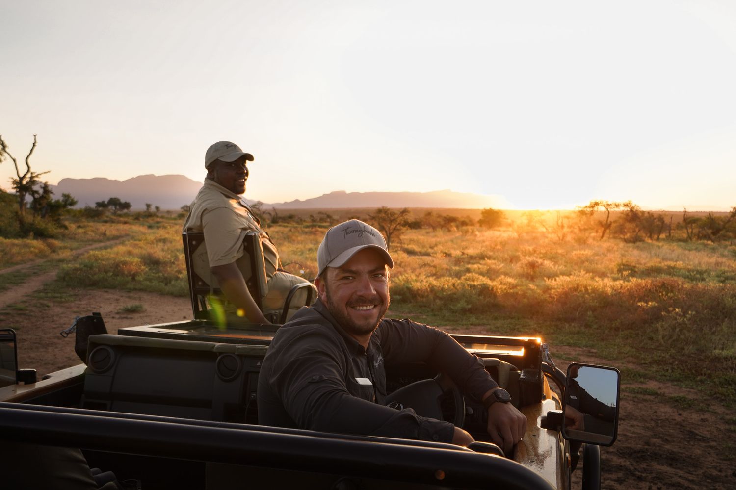 Safari vehicle driving through savanna landscape at golden hour.