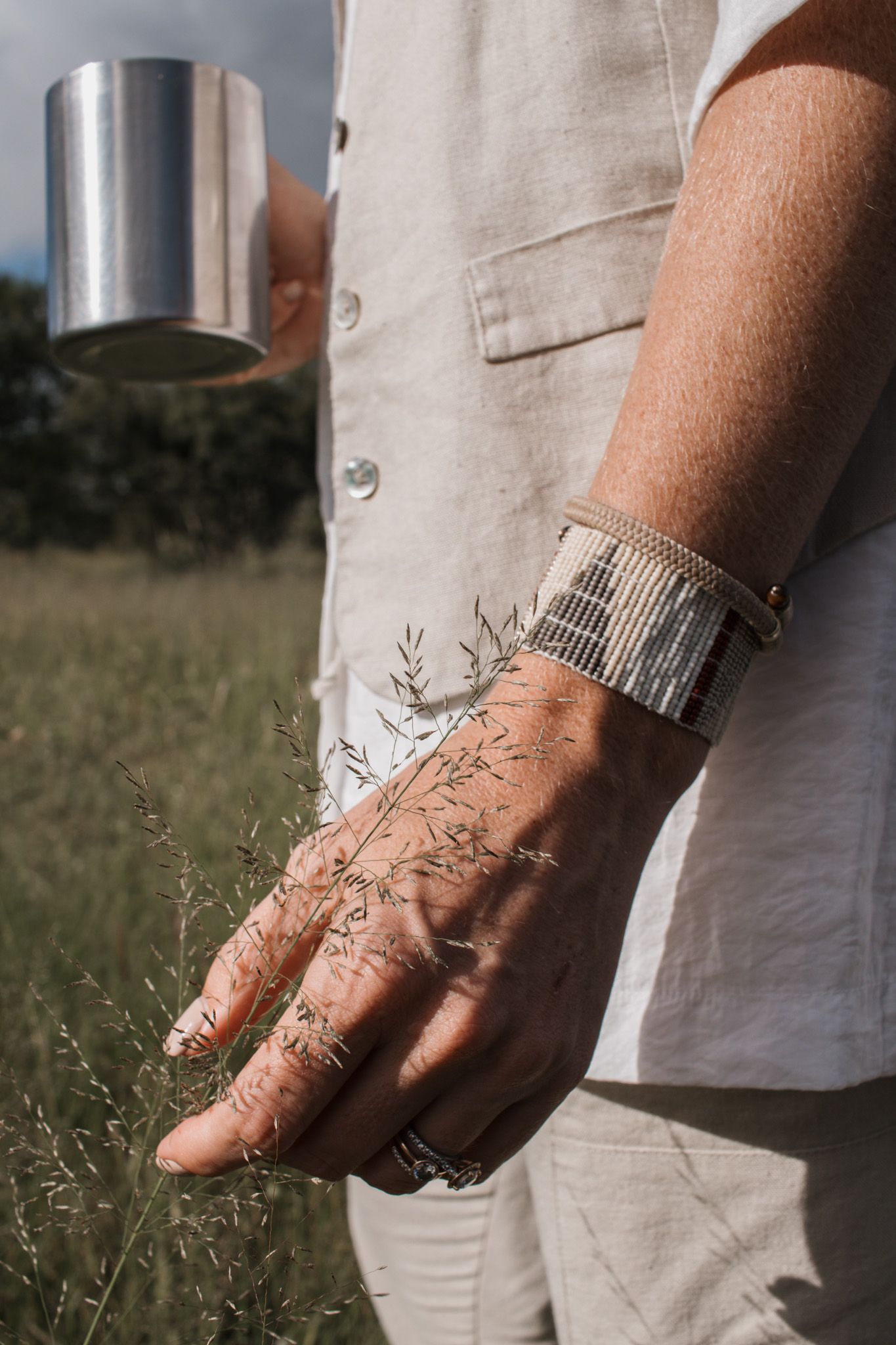 Close-up of silver bracelet and white linen clothing against grass field background.