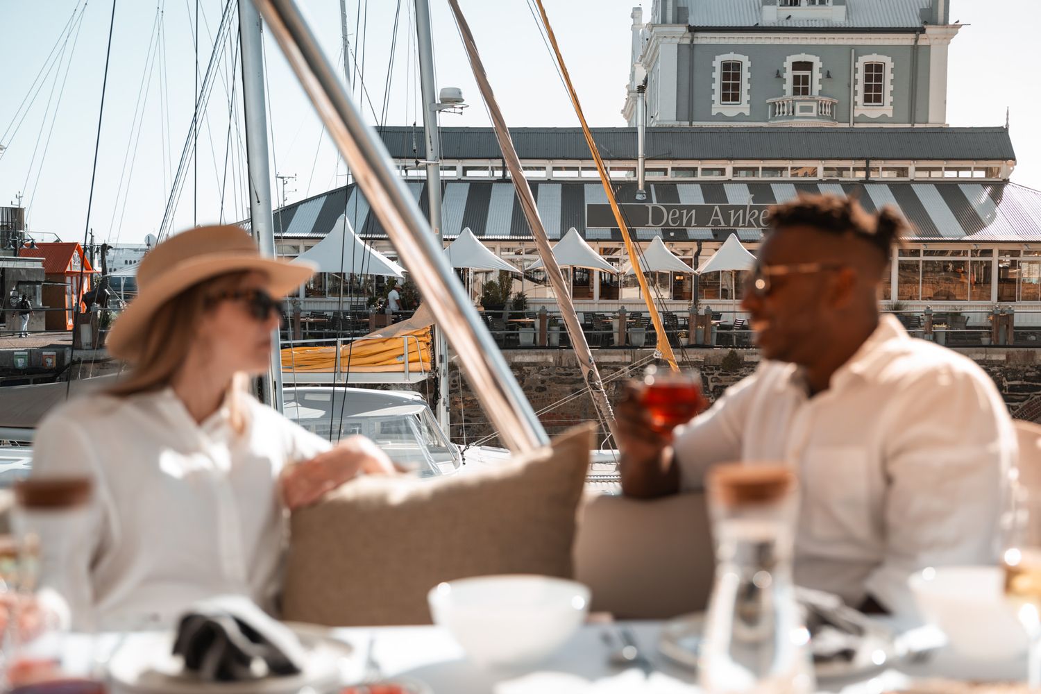 Two people enjoying drinks and conversation during an outdoor waterfront dining experience in a marina setting.