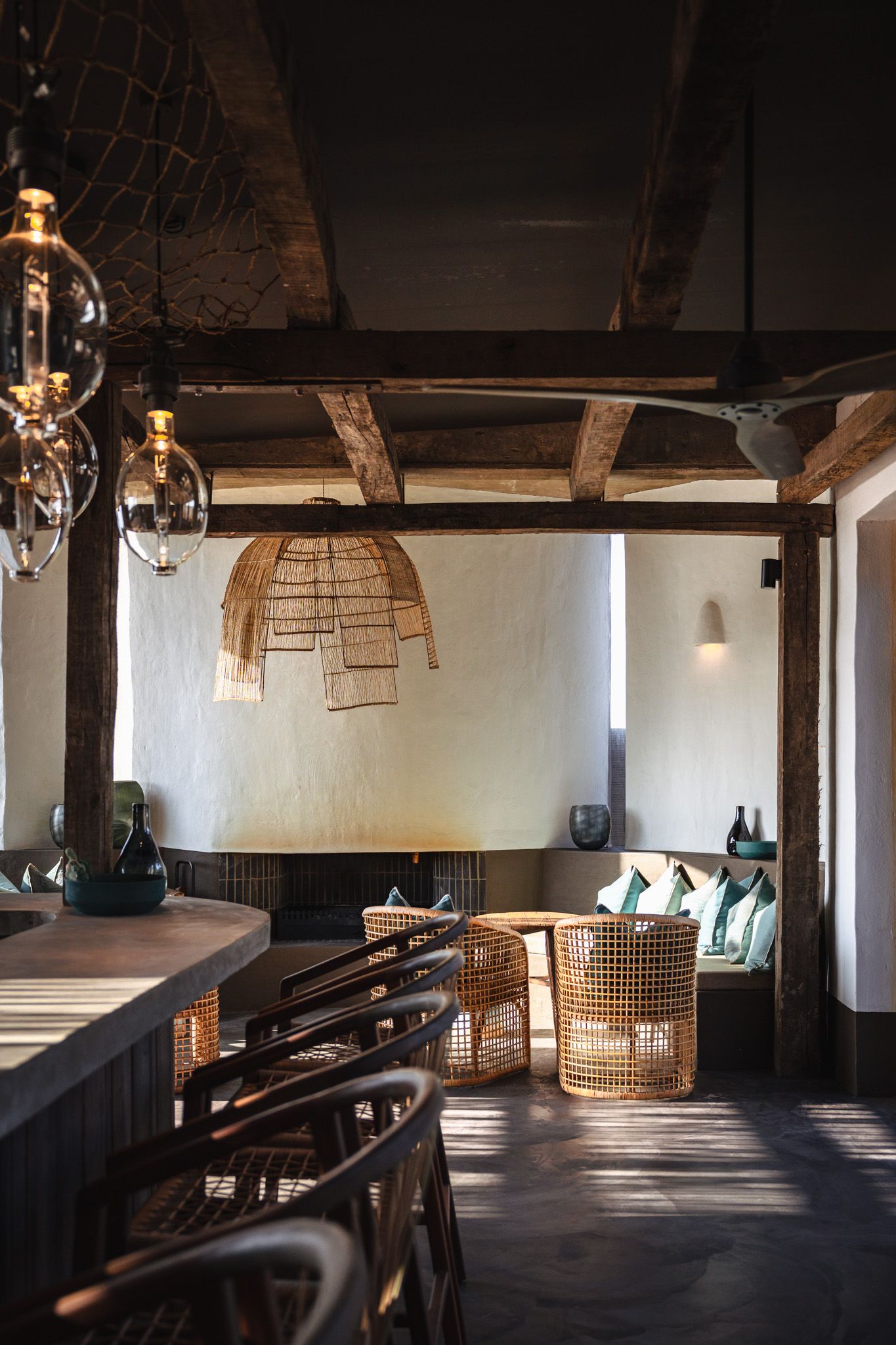 Rustic restaurant interior with rattan pendant lights, wooden beams, and cozy banquette seating.
