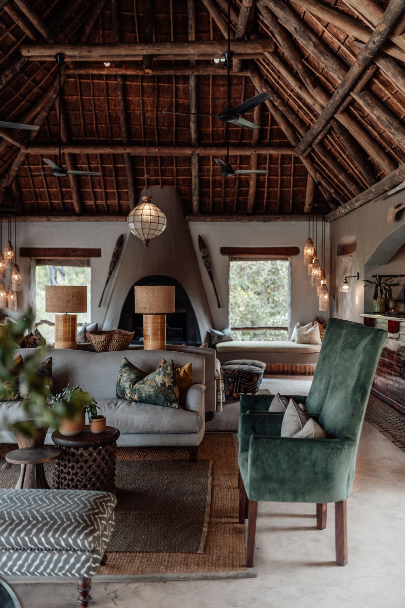 Rustic lodge living room with vaulted thatched roof, green velvet chairs and modern bohemian decor.