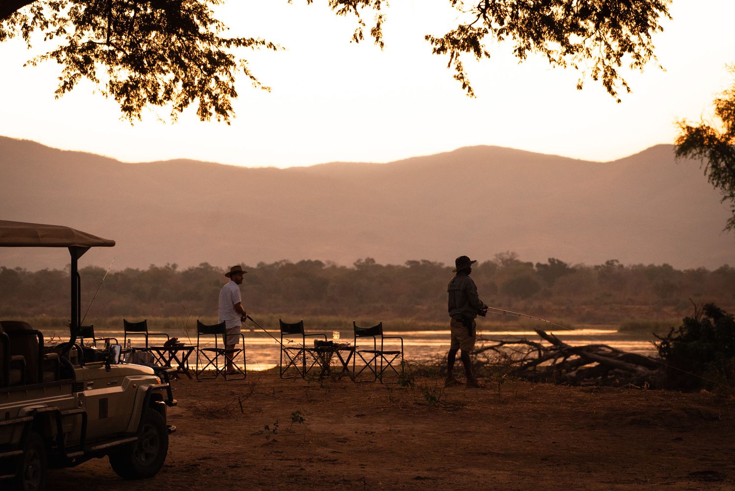 Safari lodge deck silhouetted against sunset with mountains in background.