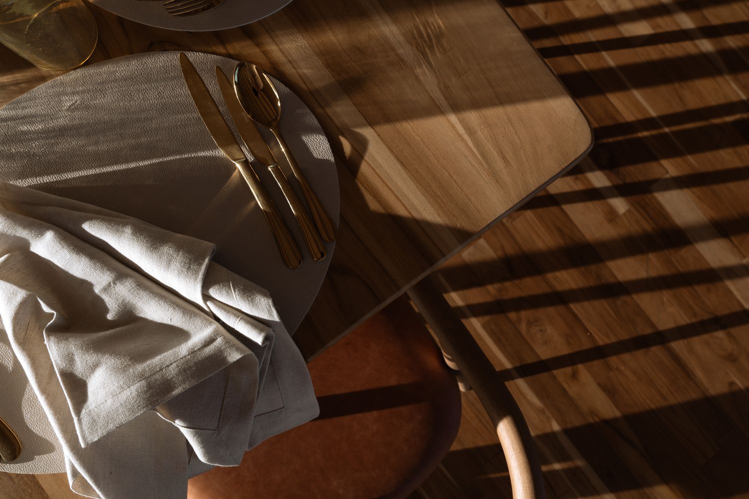 Sunlight casting dramatic shadows through window blinds onto a white cloth and wooden table.