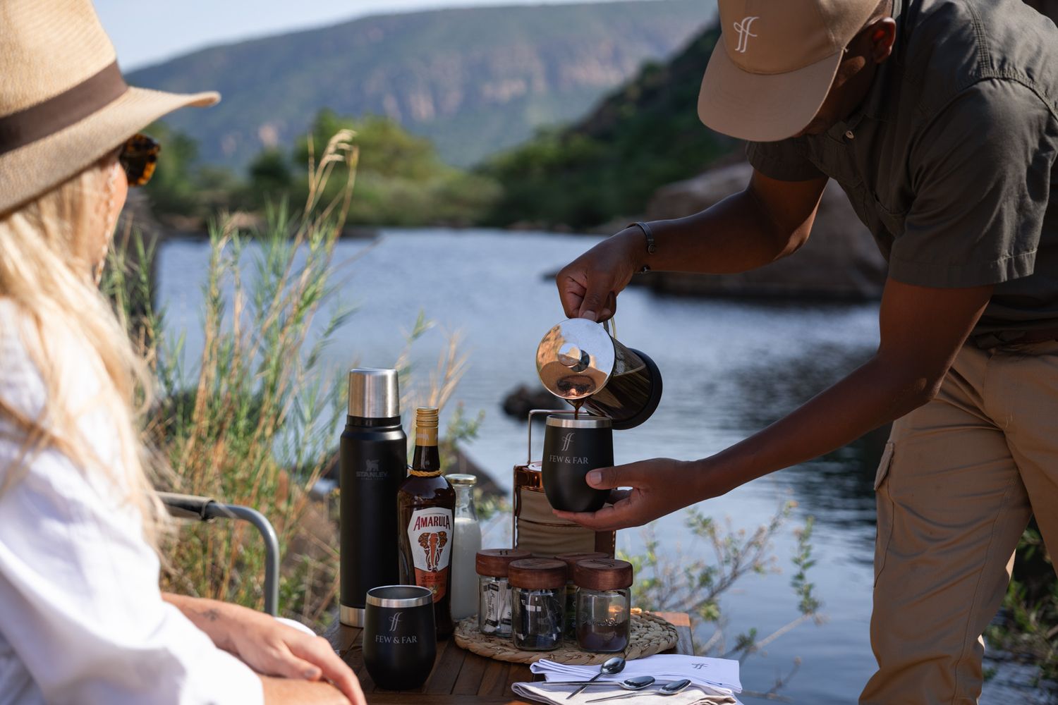 Preparing coffee outdoors by a scenic lake with camping equipment.