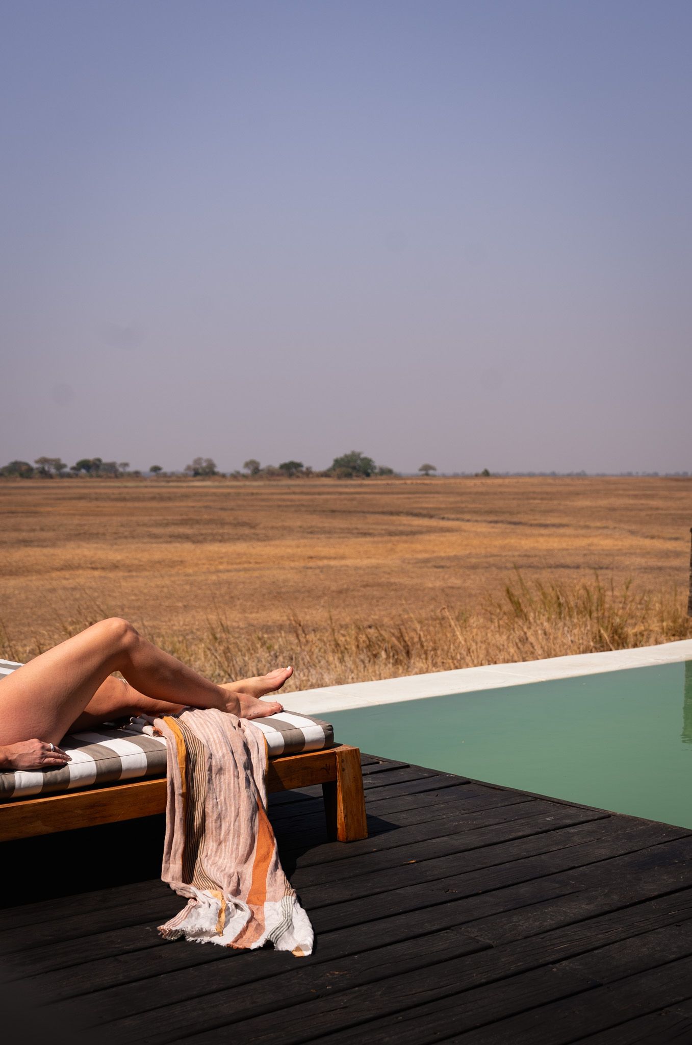 A lounger beside an infinity pool overlooking an expansive African savannah landscape.
