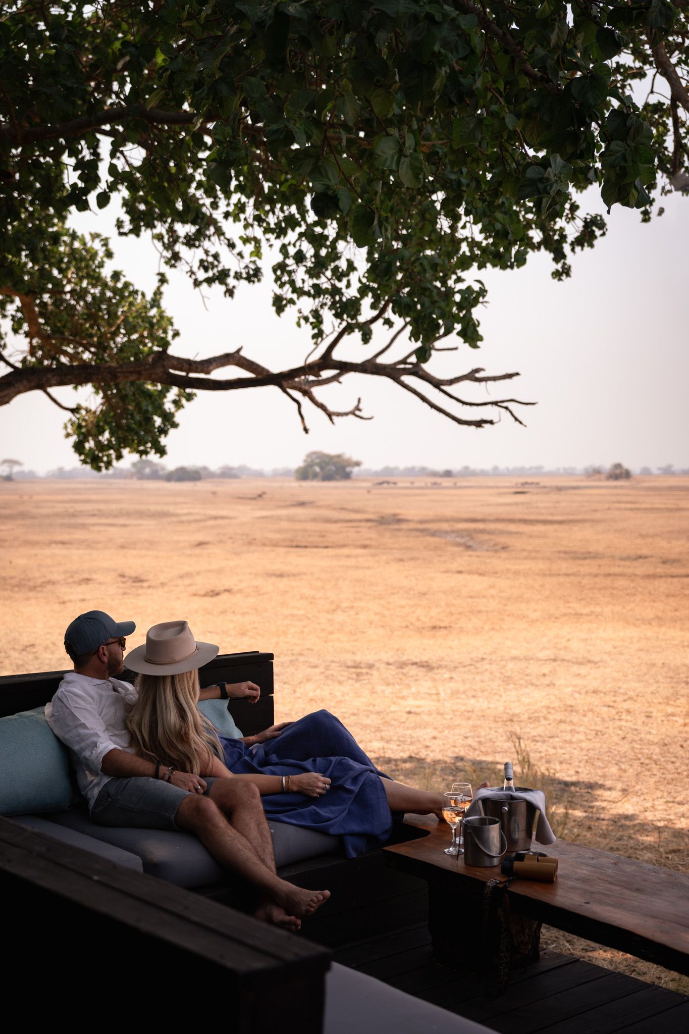 Guests lounging on outdoor deck overlooking vast African savanna landscape.