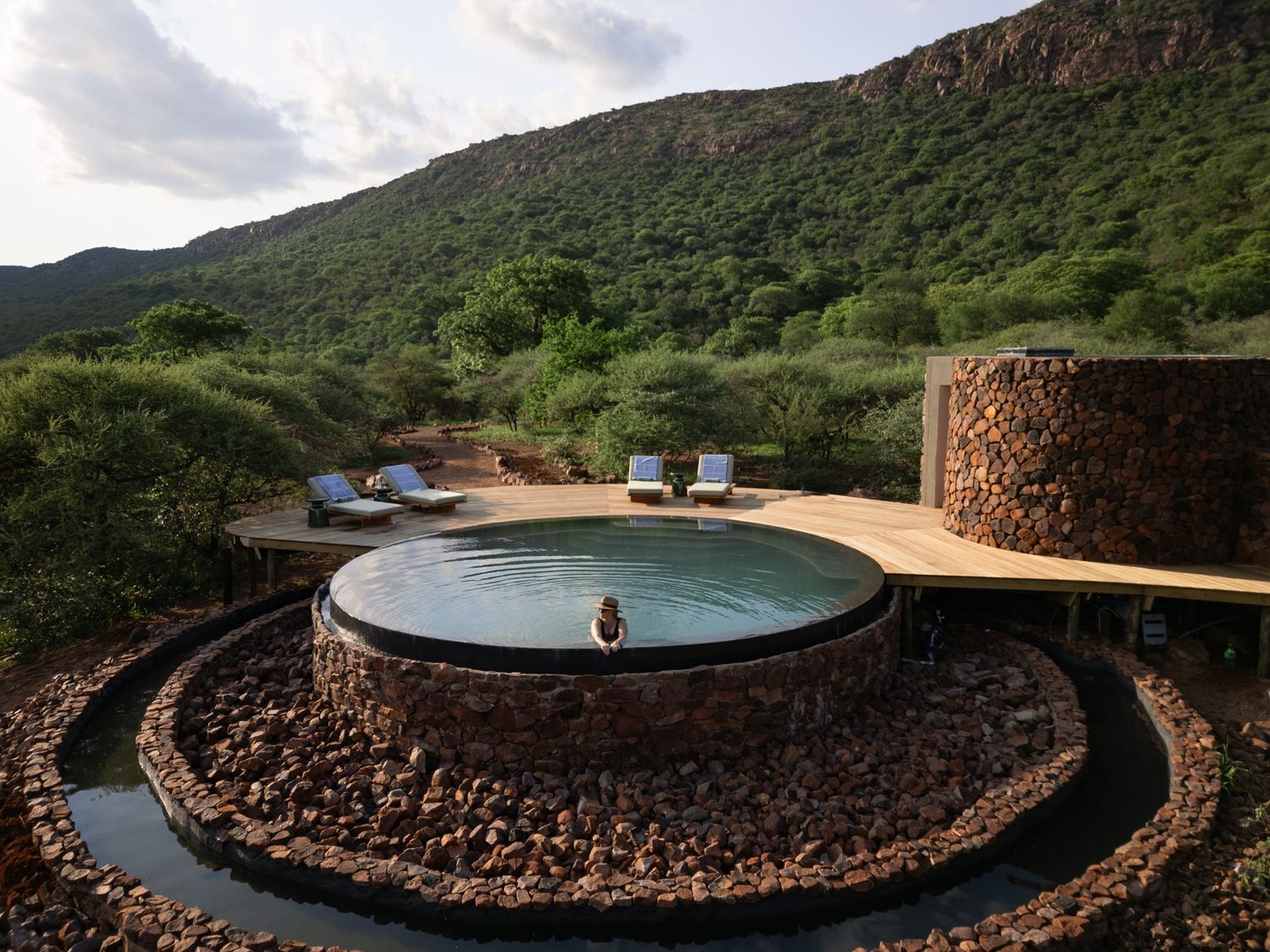 Luxurious circular plunge pool with stone surroundings overlooking mountainous landscape.