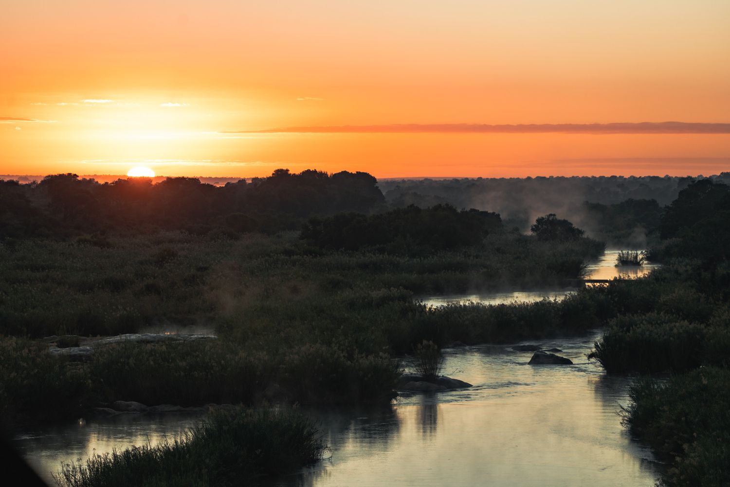 Orange sunset over winding river through marshland creating beautiful reflections.