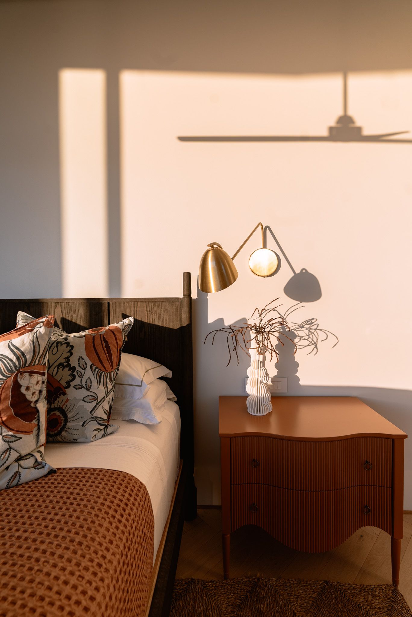 Bedroom interior with soft afternoon light casting shadows on brown bedding and wall.