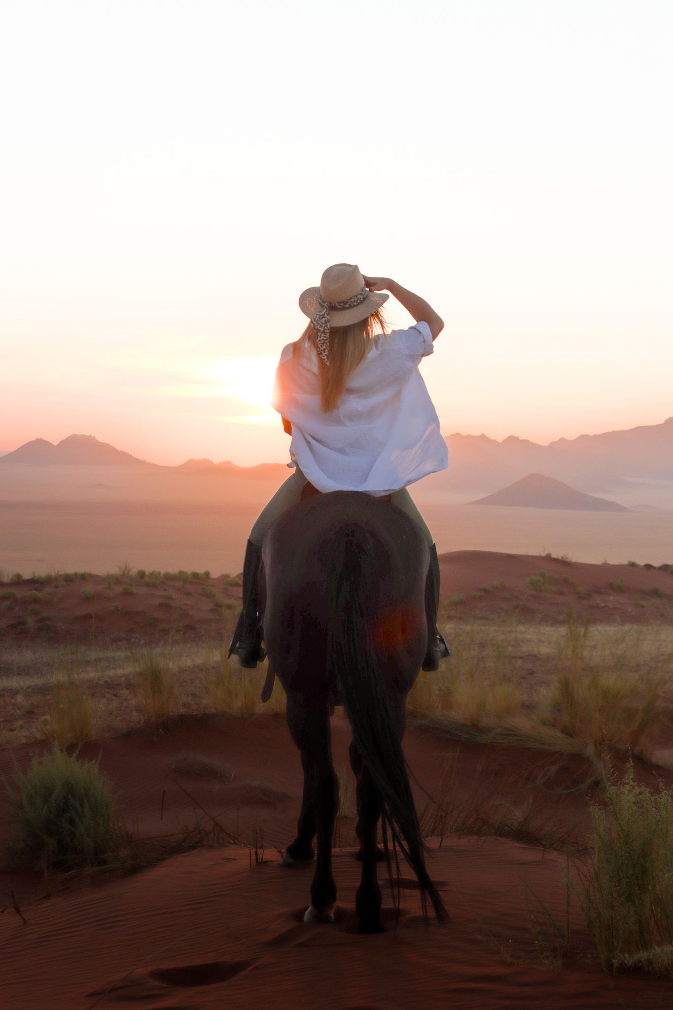 A horseback rider watching sunset over desert mountains while wearing a cowboy hat.