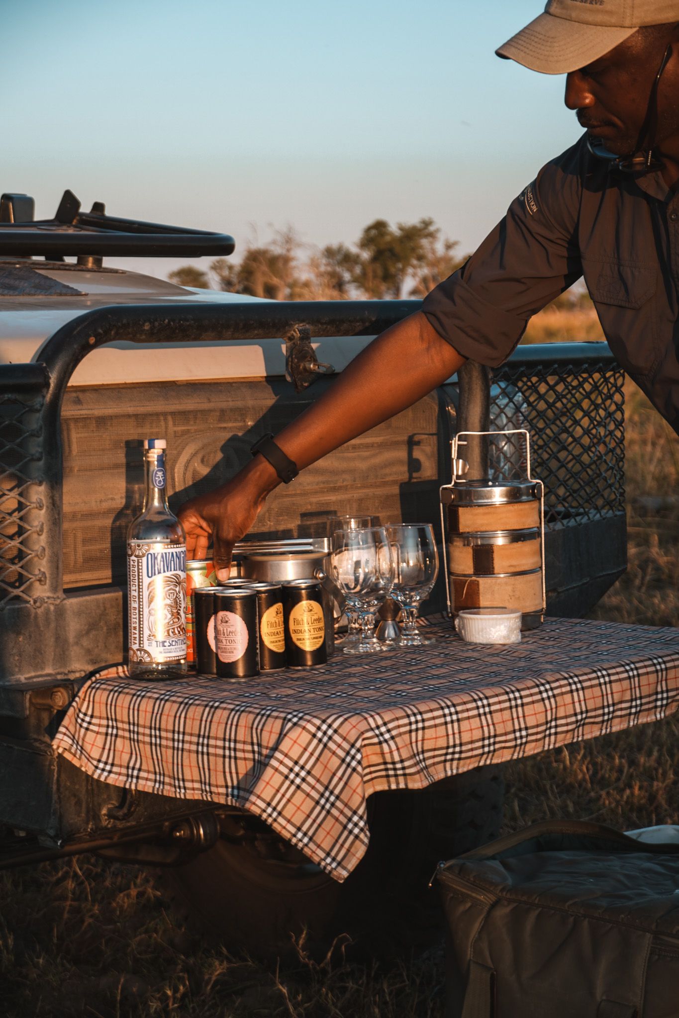 Mason jars and glasses arranged on a plaid tablecloth for outdoor dining at sunset.