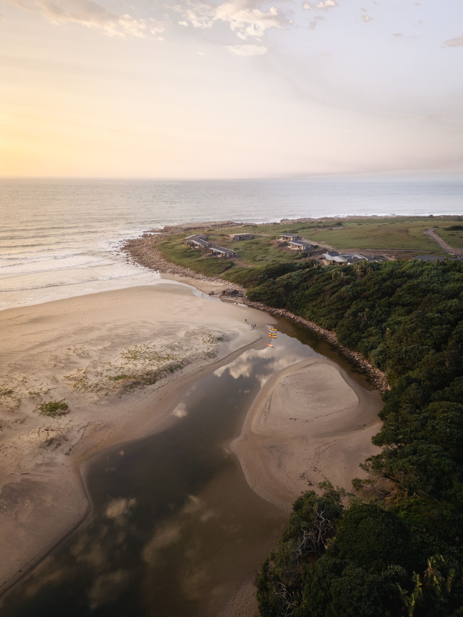Aerial view of a curved coastline with beach houses and sand formations during golden sunset.