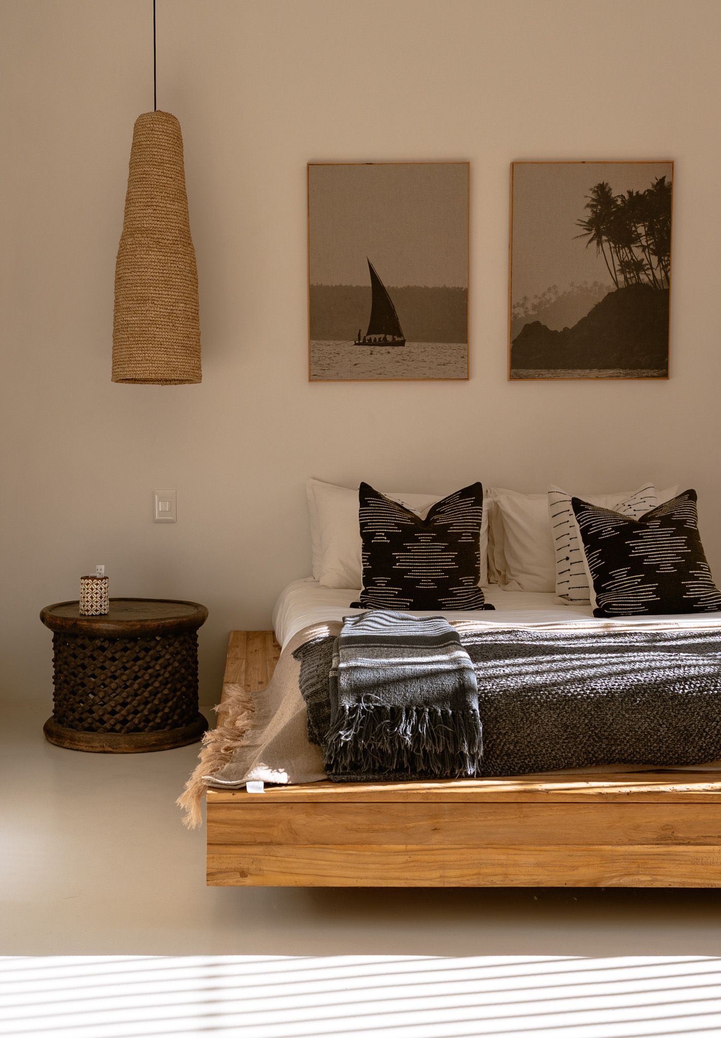 Bohemian bedroom with wooden platform bed, woven pendant light, and black and white artwork.