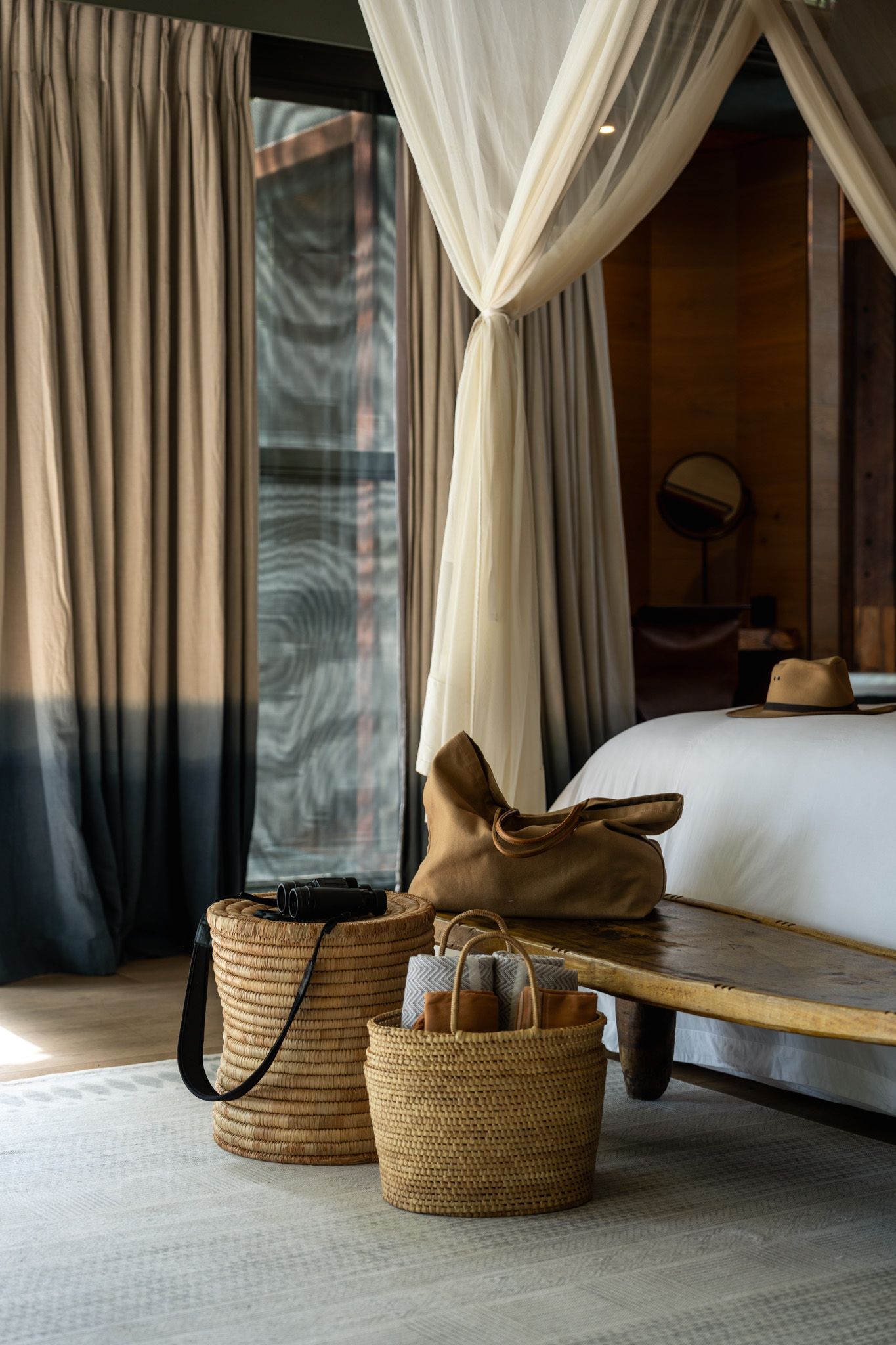 Woven baskets and white curtains beside a minimalist bed in a serene bedroom.