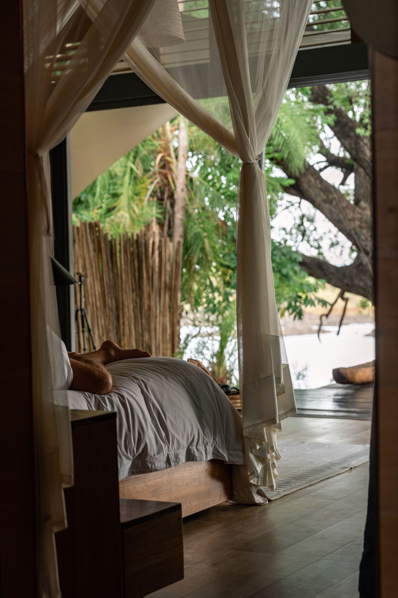 Tranquil bedroom with flowing white curtains and tropical garden view.