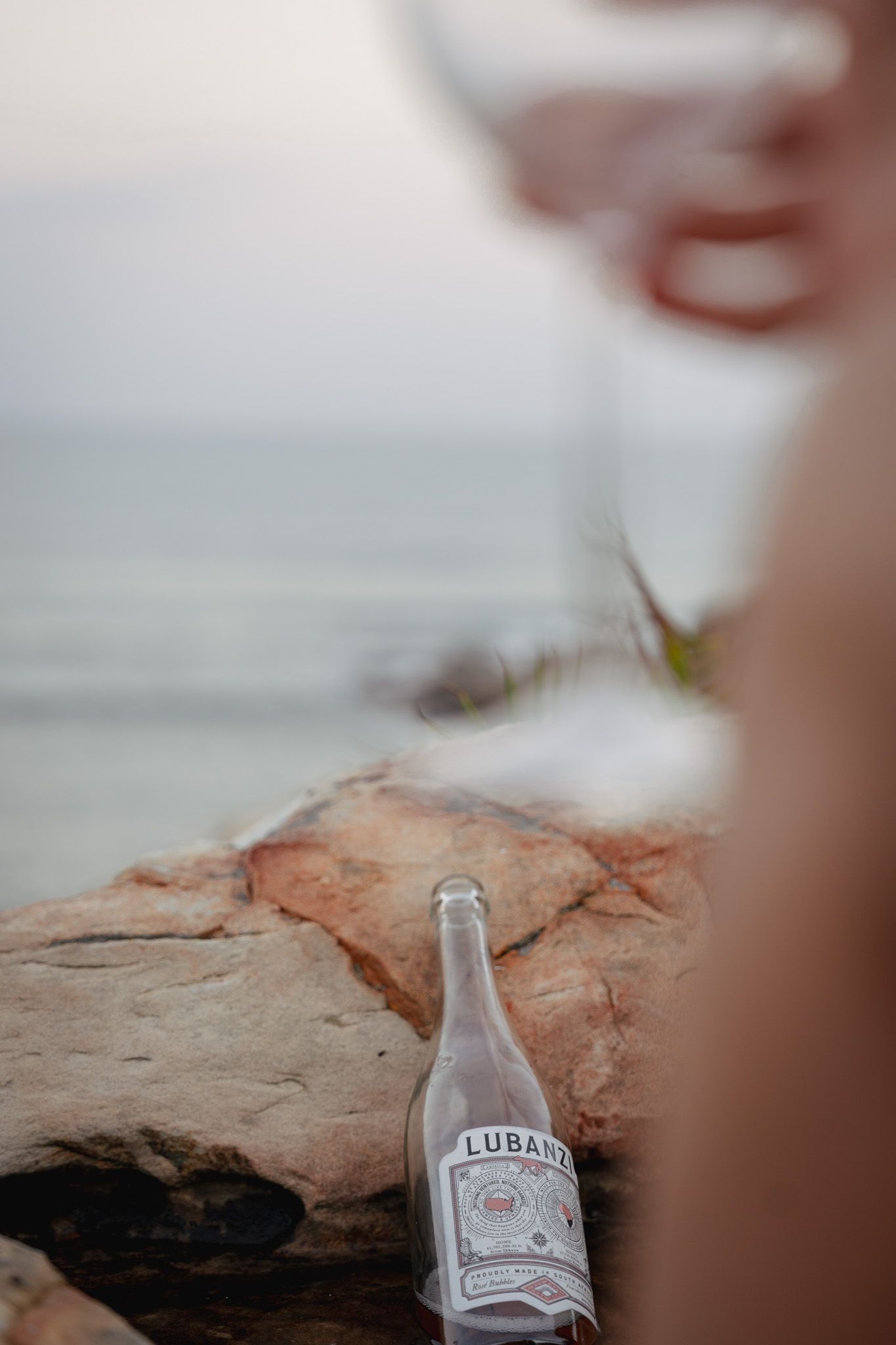 Empty glass bottle on rocky coastal outcrop with blurred ocean background.