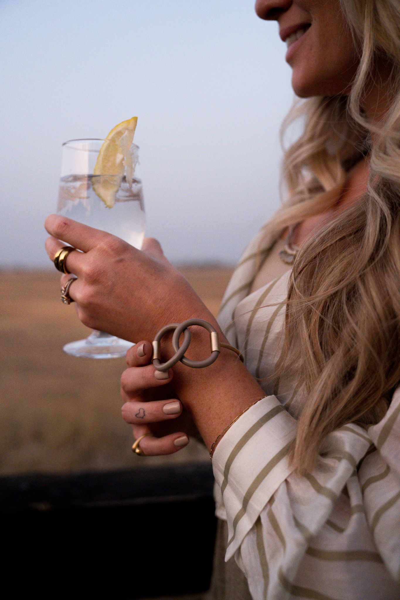 Woman holding a cocktail with a citrus garnish in a desert setting at sunset.