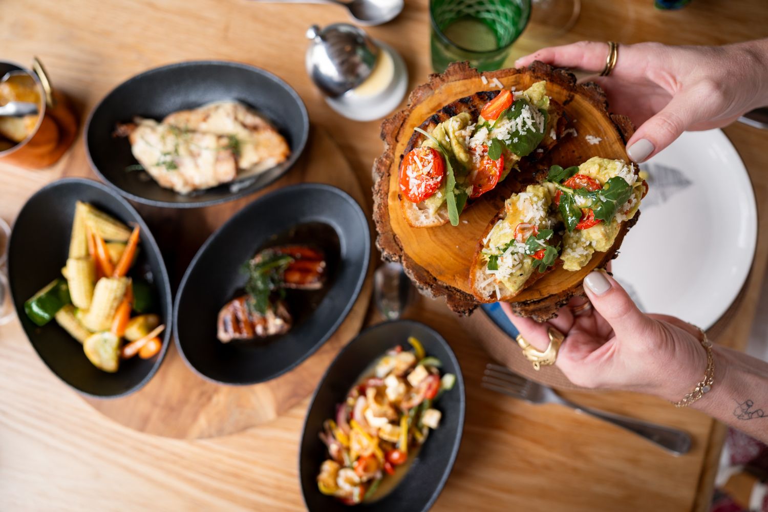 Hands reaching for various appetizer plates on wooden dining table.