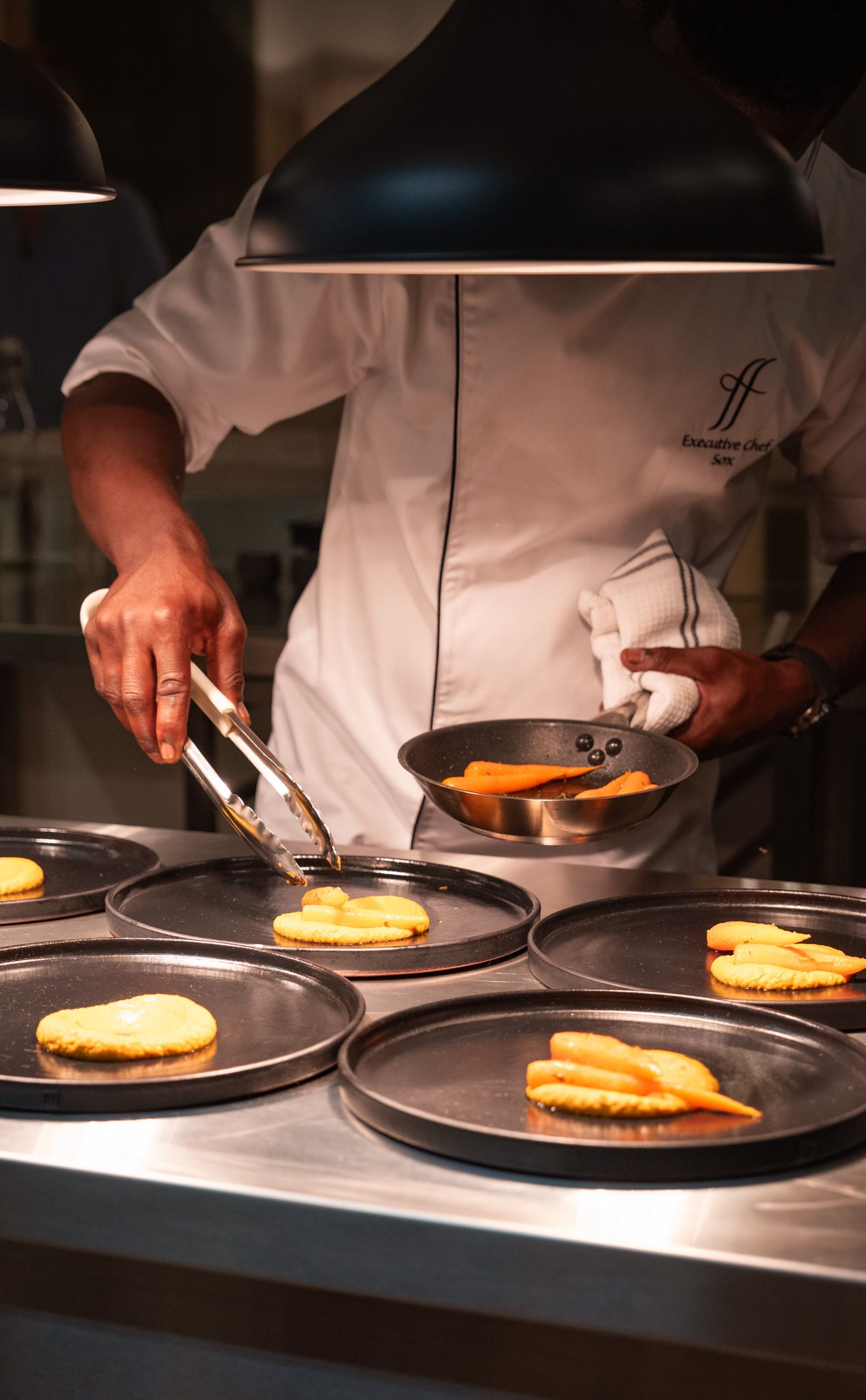 Chef cooking multiple pancakes on dark plates in professional kitchen.