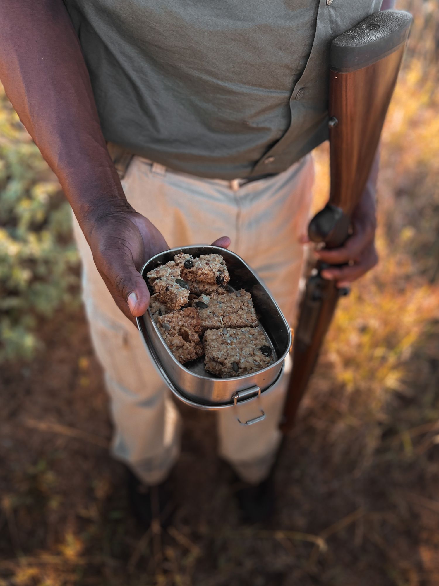 Close-up of hands holding metal container with baked treats outdoors.