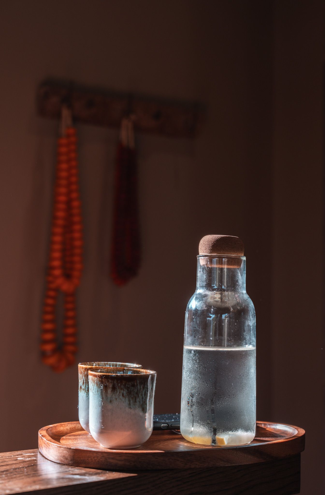 Glass water vessels on wooden tray with condensation in moody lighting.