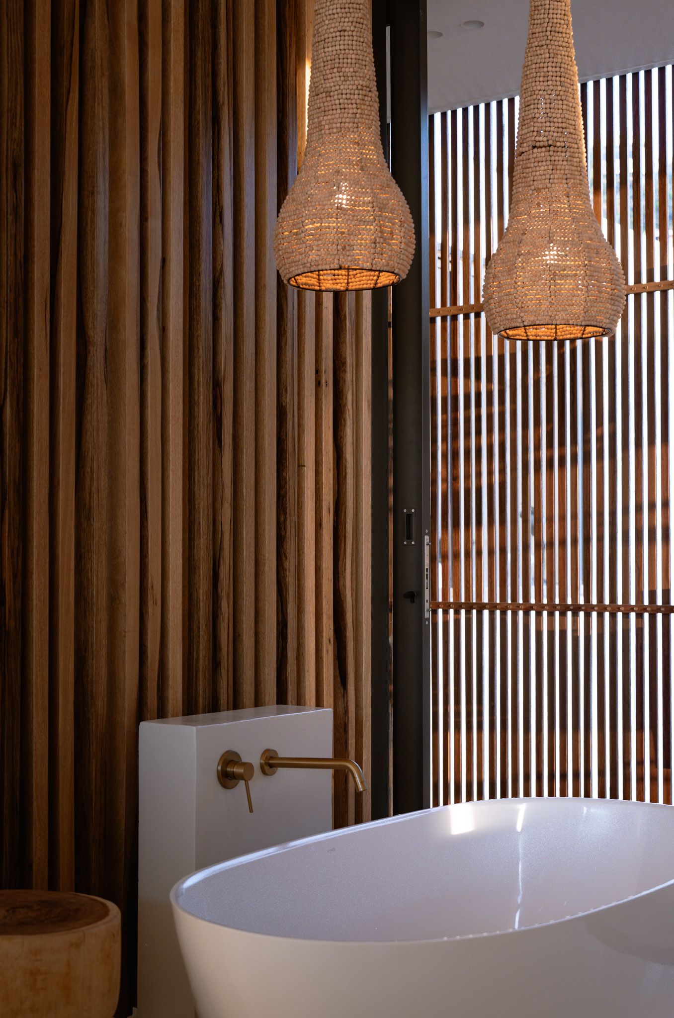Modern bathroom with woven pendant lights and freestanding tub against wooden slat wall.