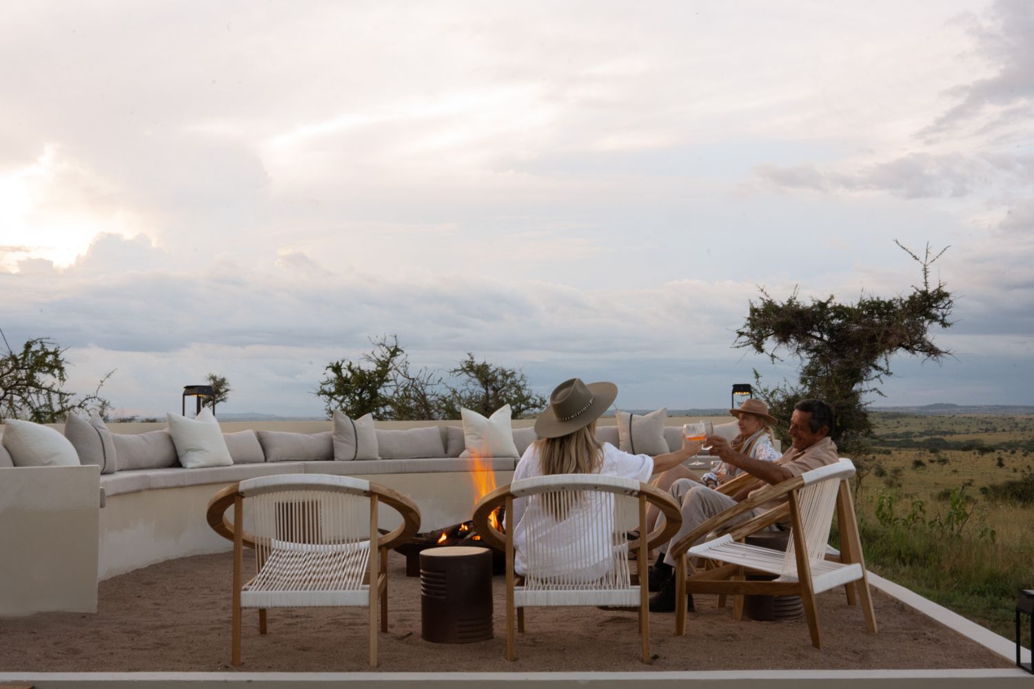 Outdoor lounge area with comfortable seating and fire pit overlooking vast plains at dusk.
