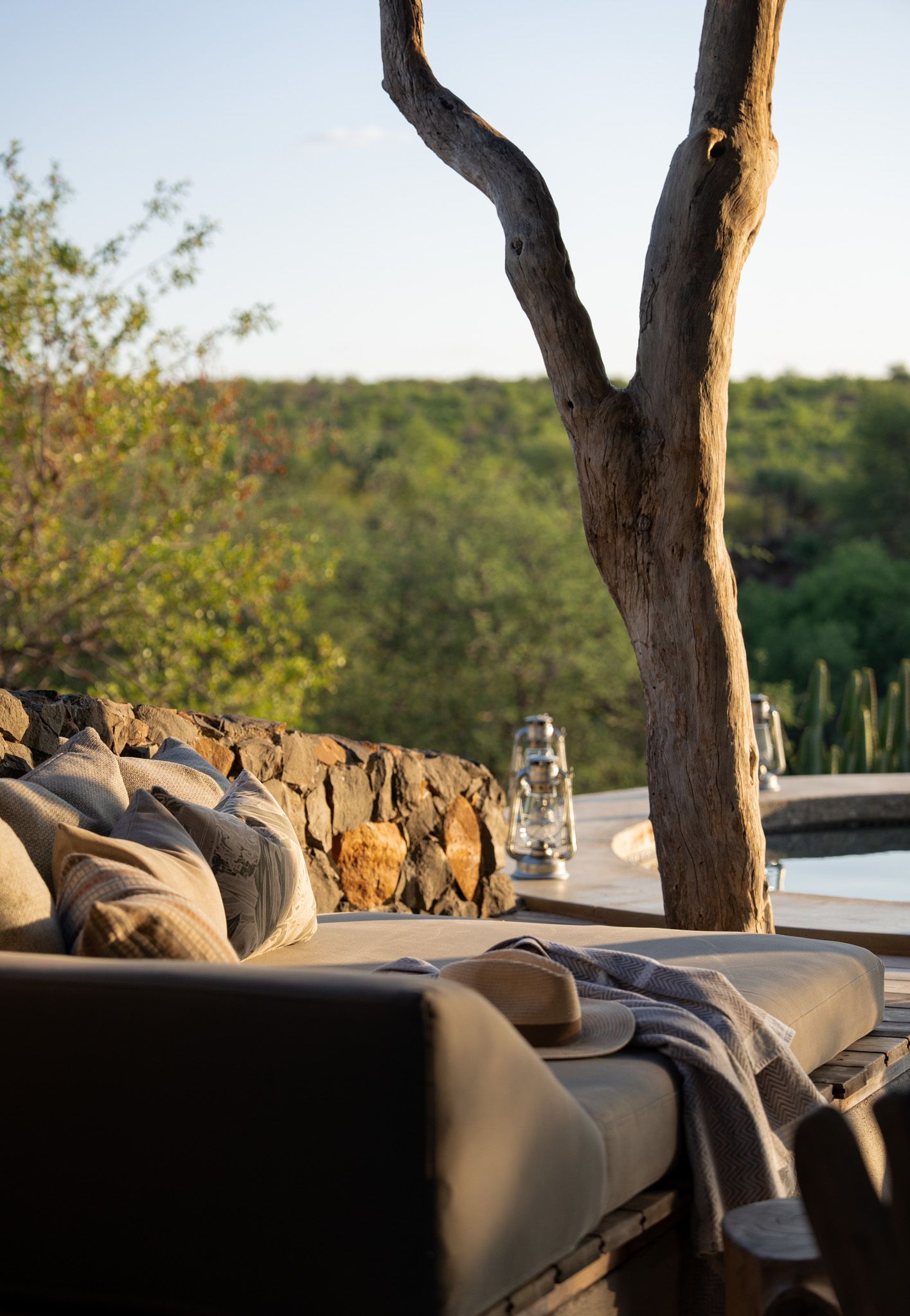 Luxury canvas camping bed with comfortable pillows and linens overlooks a scenic natural landscape at sunset.